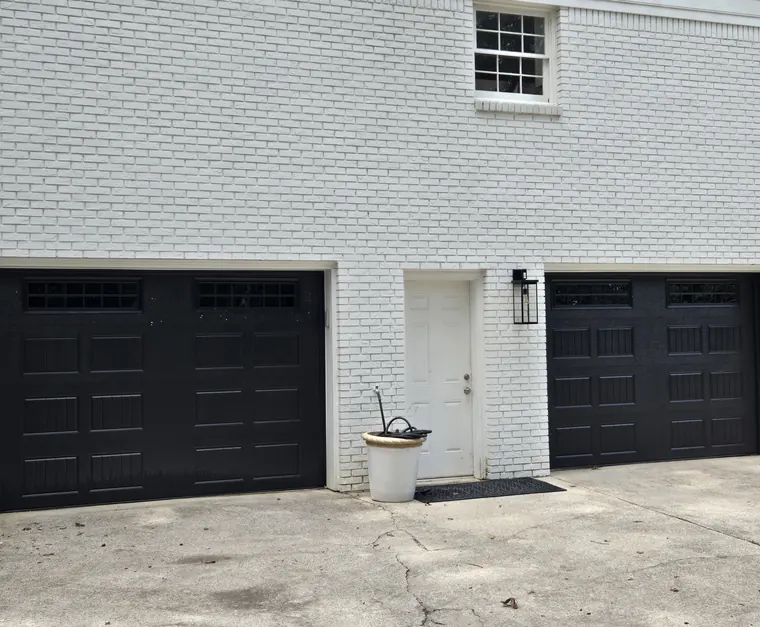 A white brick house with two new black garage doors, each with a row of windows