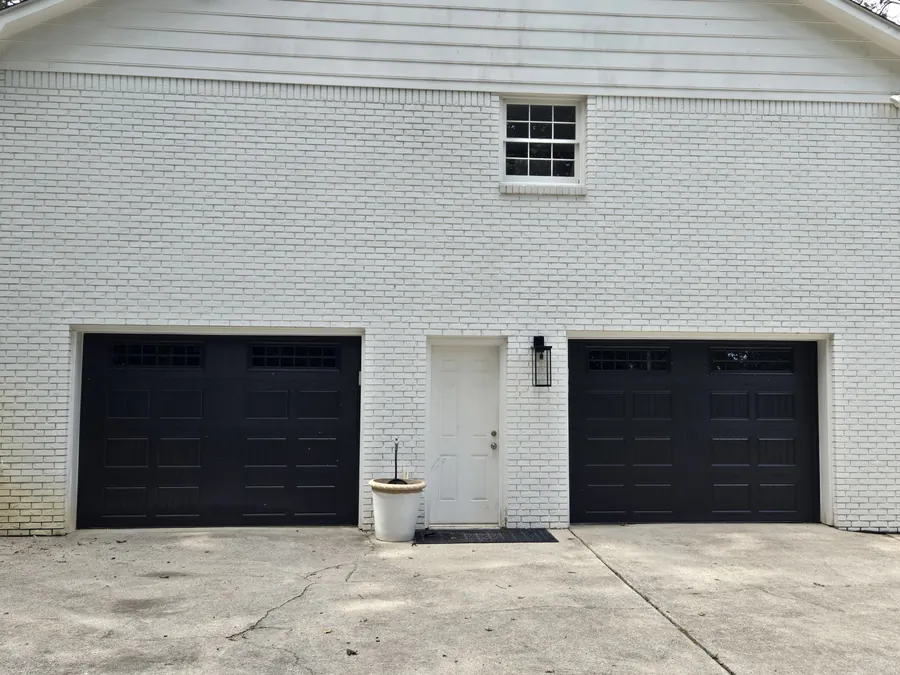 A white brick house with two new black garage doors and a white side door between them