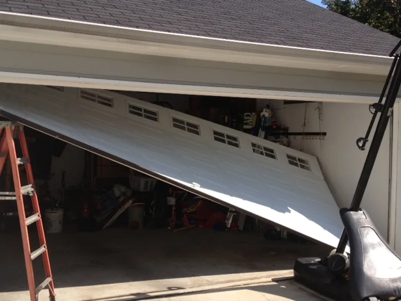 A garage door knocked crooked in its opening, one side hanging out of the track