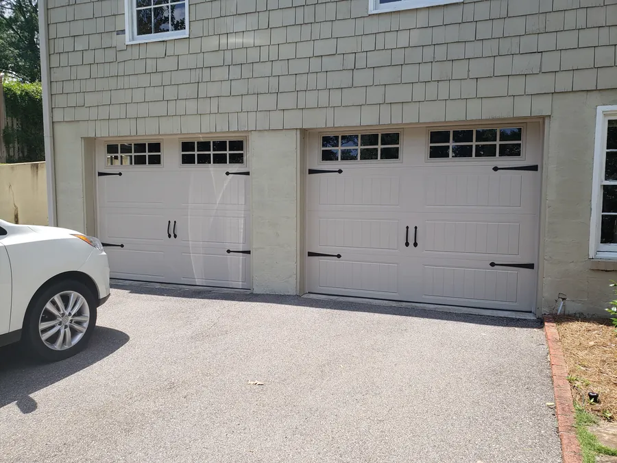 Two new tan carriage-style garage doors with black handles and hinges and a row of windows
