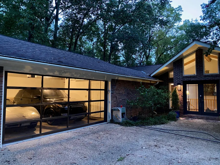 A full-view glass and black aluminum garage door at dusk, lit from inside